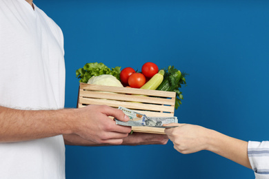 Photo of Client paying courier for fresh products on blue background, closeup. Food delivery service