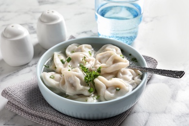 Photo of Bowl of tasty dumplings in broth with spoon on white marble table