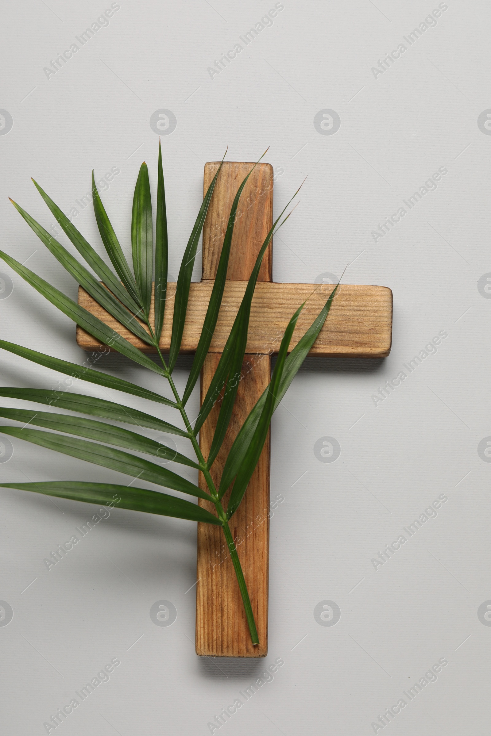 Photo of Wooden cross and palm leaf on light grey background, top view. Easter attributes