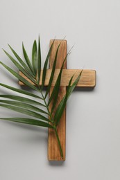 Wooden cross and palm leaf on light grey background, top view. Easter attributes