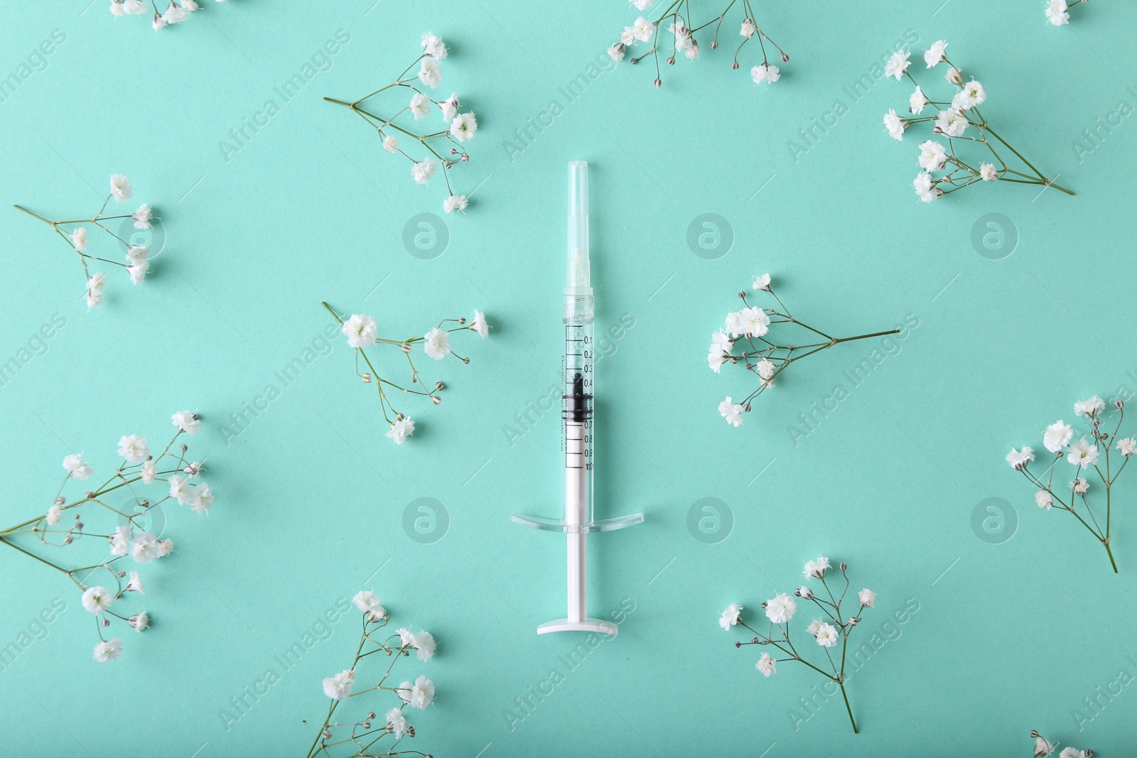 Photo of Cosmetology. Medical syringe and gypsophila flowers on turquoise background, flat lay