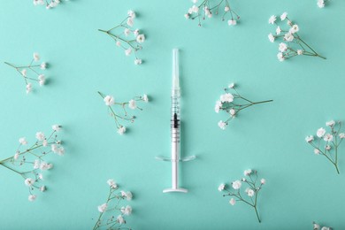 Cosmetology. Medical syringe and gypsophila flowers on turquoise background, flat lay