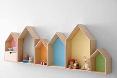 Photo of Different house shaped shelves with toys on white wall. Interior design