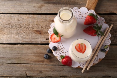 Photo of Tasty yogurt in glass, bottle, straws and berries on wooden table, top view. Space for text