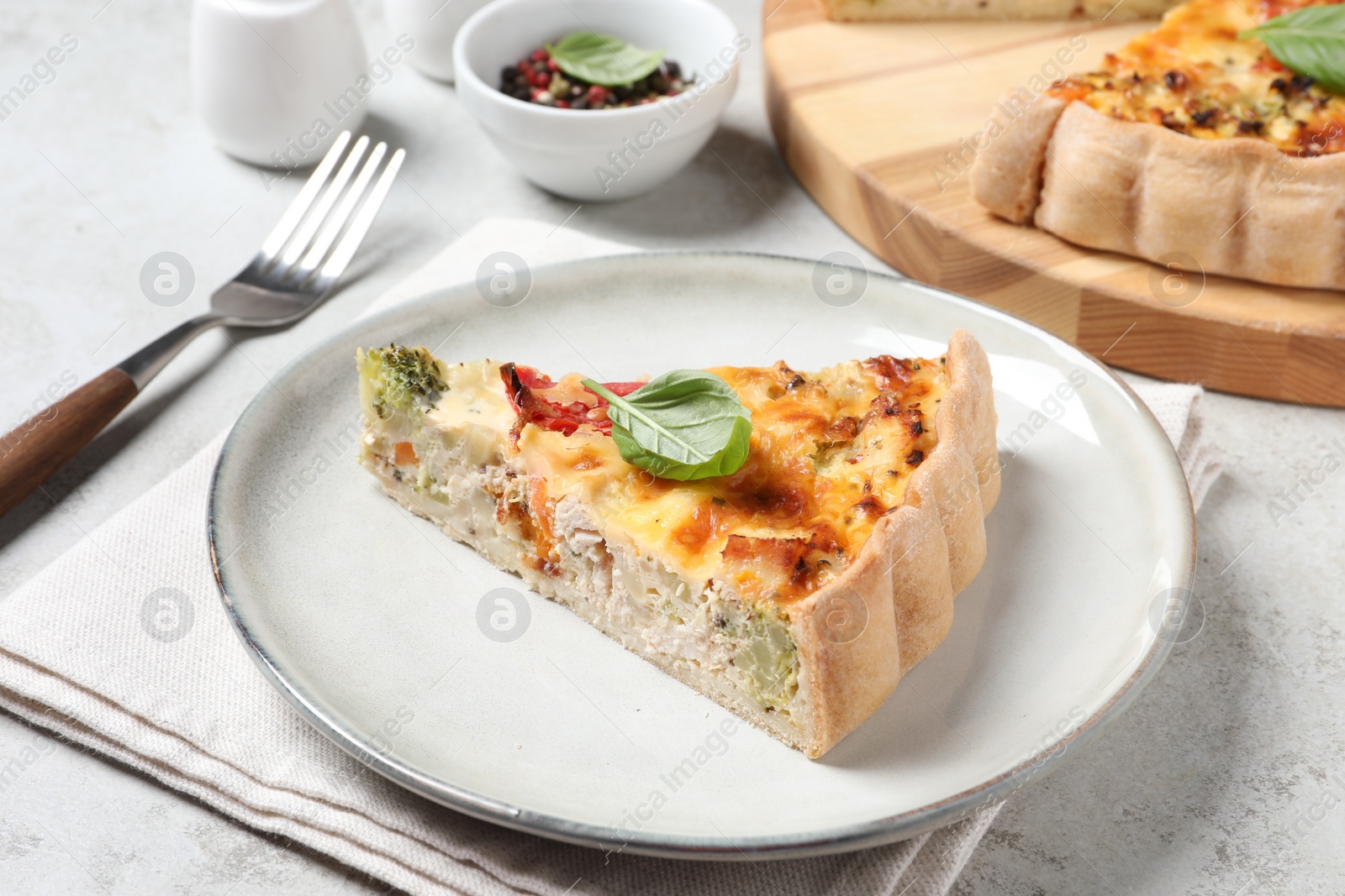 Photo of Piece of tasty quiche with chicken, vegetables, basil and cheese served on light table, closeup