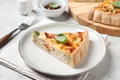 Piece of tasty quiche with chicken, vegetables, basil and cheese served on light table, closeup