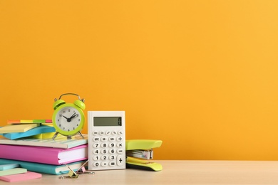 Different school stationery and alarm clock on table against orange background, space for text. Back to school