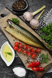 Photo of Delicious smoked mackerel and different products on black textured table, flat lay