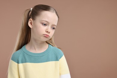 Portrait of sad girl on light brown background, space for text