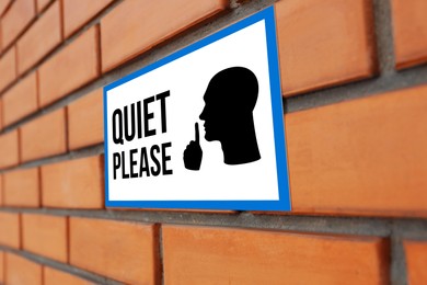 Image of Quiet Please sign with shush gesture image on orange brick wall, closeup