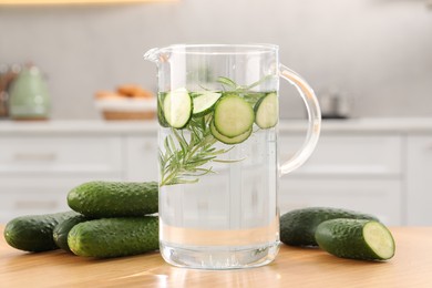 Photo of Refreshing cucumber water with rosemary in jug and vegetable on wooden table