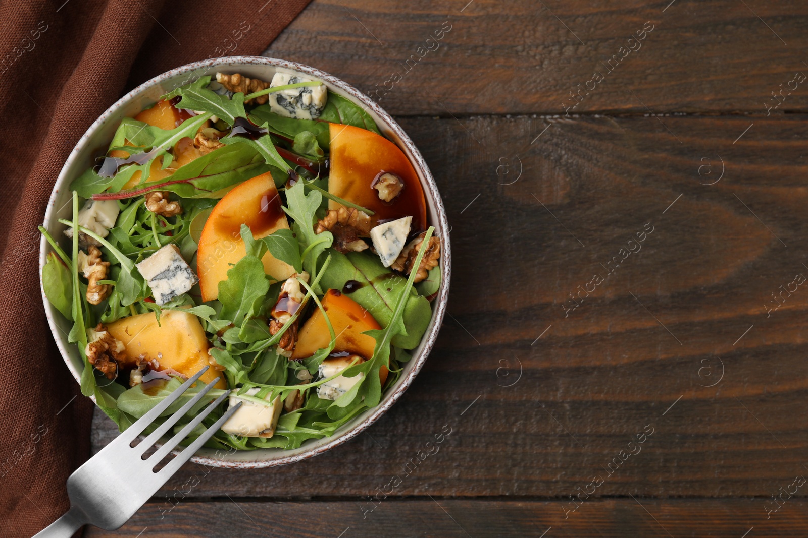 Photo of Tasty salad with persimmon, blue cheese and walnuts served on wooden table, top view. Space for text