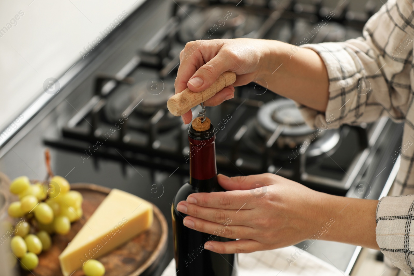 Photo of Woman opening wine bottle with corkscrew at countertop indoors, closeup