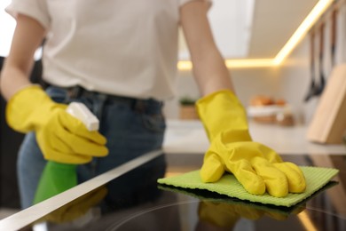 Woman with spray bottle and microfiber cloth cleaning electric stove in kitchen, closeup