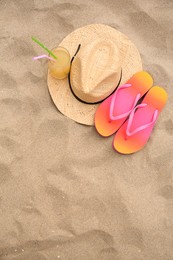 Photo of Straw hat, flip flops and refreshing drink on sand, flat lay with space for text. Beach accessories