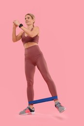 Photo of Woman exercising with elastic resistance band on pink background, low angle view