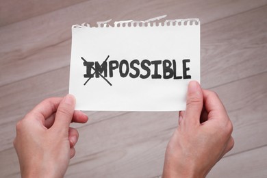 Photo of Motivation concept. Woman holding paper with changed word from Impossible into Possible by crossing over letters I and M indoors, closeup
