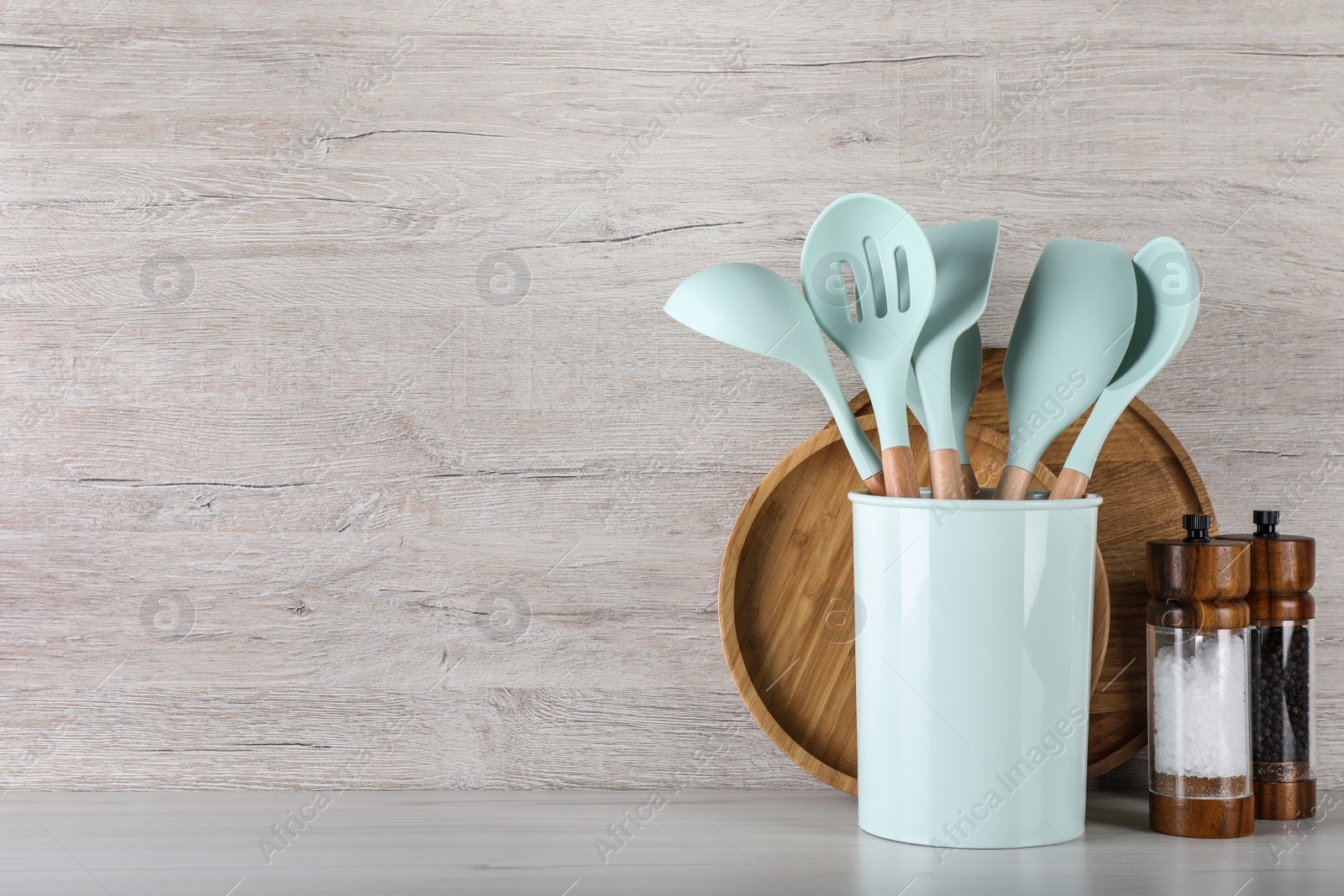 Photo of Holder with kitchen utensils, spice shakers and serving boards on white wooden table. Space for text