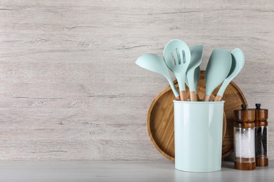 Photo of Holder with kitchen utensils, spice shakers and serving boards on white wooden table. Space for text