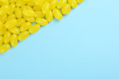 Photo of Many delicious lemon jelly beans on light blue background, flat lay. Space for text