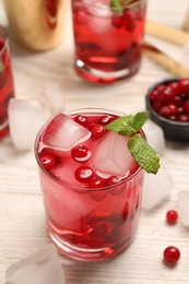Tasty cranberry cocktail with ice cubes and mint in glasses on wooden table, closeup