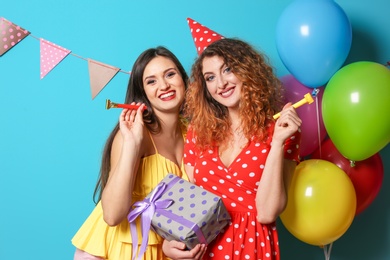 Young women with party blowers and gift box on color background. Birthday celebration