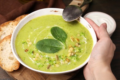 Photo of Woman with bowl of delicious broccoli cream soup at table, closeup