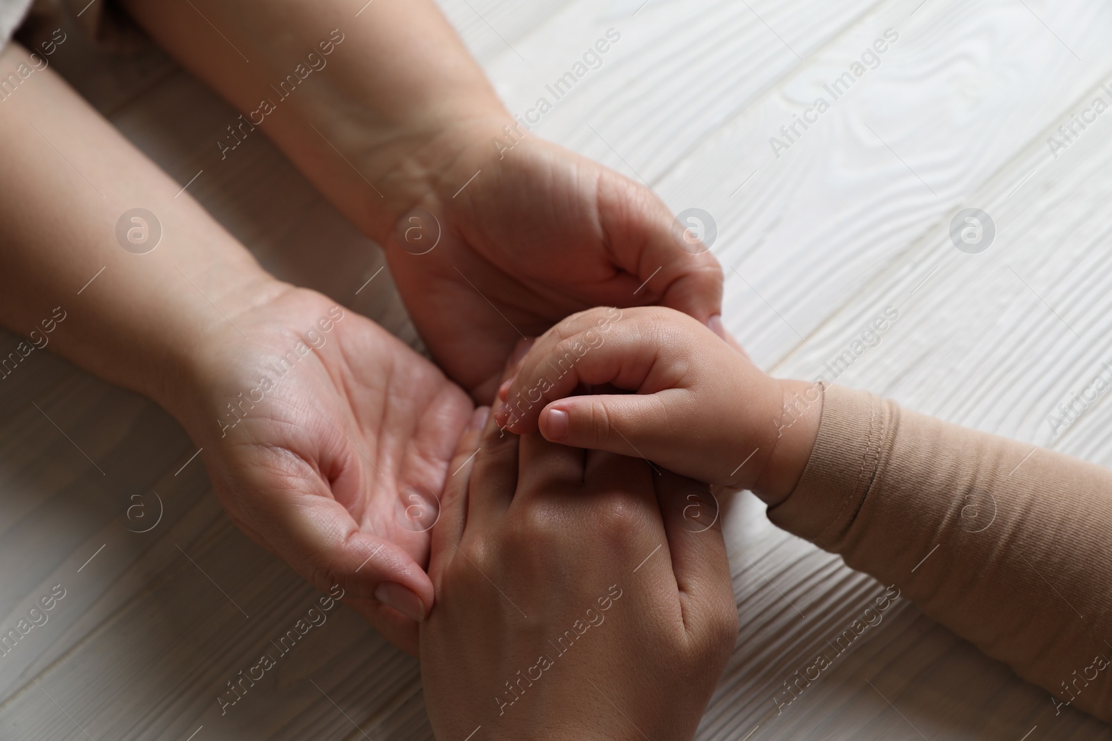 Photo of Family holding hands together at white wooden table, above view