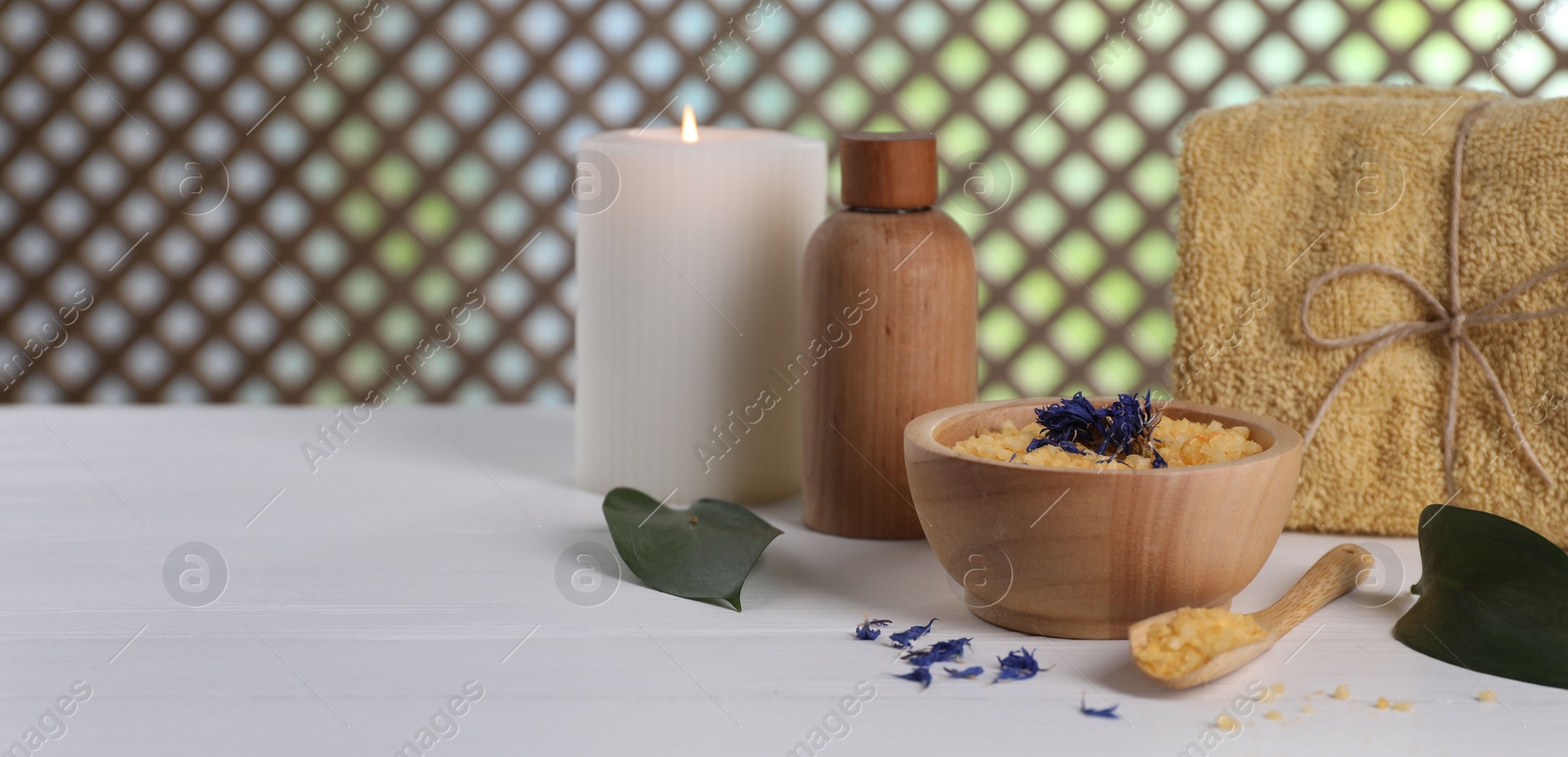 Photo of Spa composition. Sea salt, bottle of cosmetic product, towel and burning candle on white table, space for text