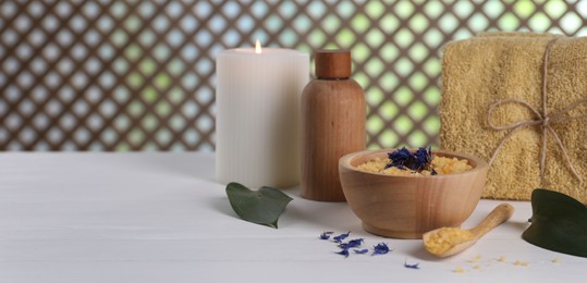 Spa composition. Sea salt, bottle of cosmetic product, towel and burning candle on white table, space for text