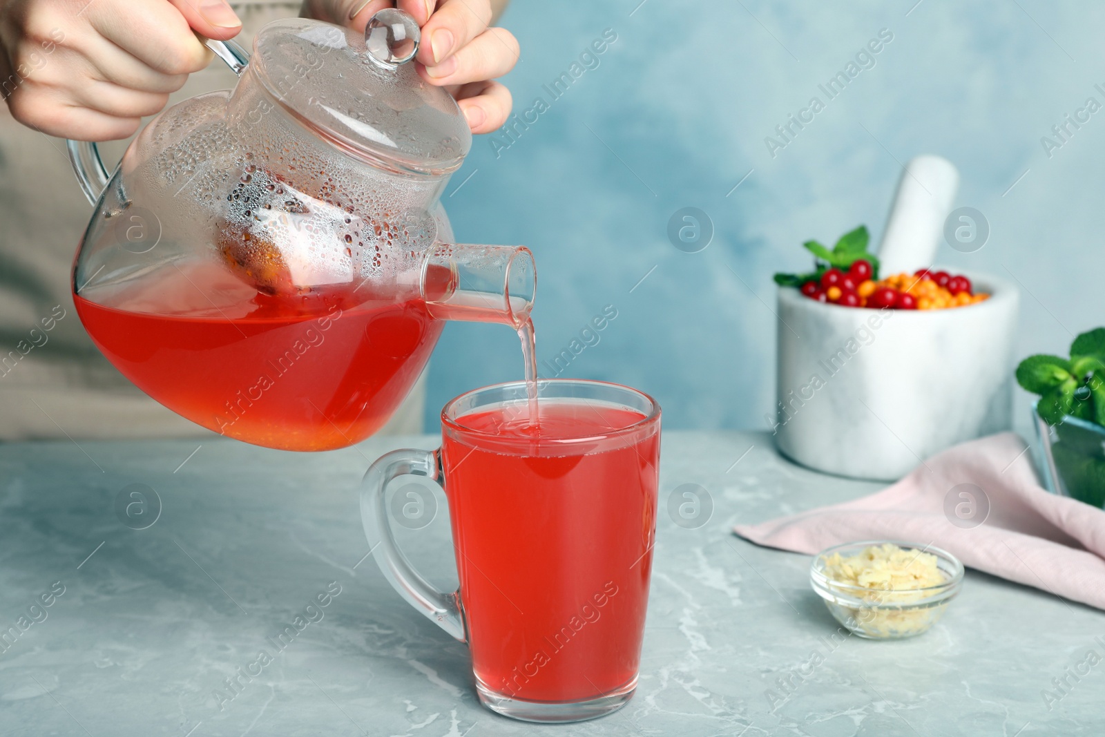 Photo of Woman pouring immunity boosting drink into cup at light grey marble table, closeup