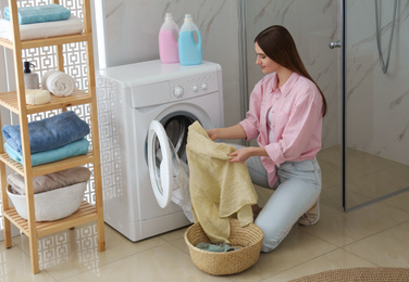 Young woman with clothes near washing machine in bathroom. Laundry day