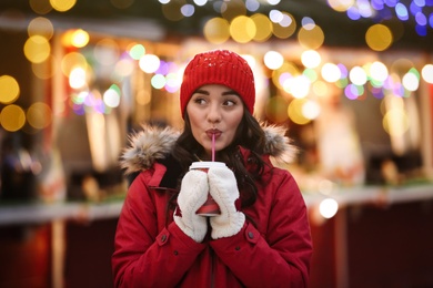 Photo of Happy young woman with cup of drink on city street in evening. Christmas celebration