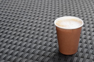 Photo of Cardboard cup with coffee on rattan surface, space for text