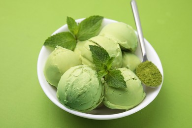 Photo of Tasty matcha ice cream and spoon with powder in bowl on green table