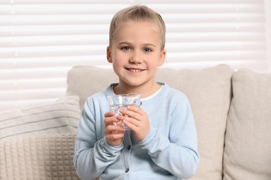 Photo of Happy little girl holding glass of fresh water indoors