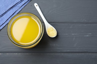 Glass jar and spoon of Ghee butter on grey wooden table, flat lay. Space for text