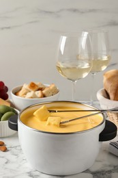 Photo of Pot of tasty cheese fondue, snacks and wine on white marble table