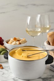 Pot of tasty cheese fondue, snacks and wine on white marble table