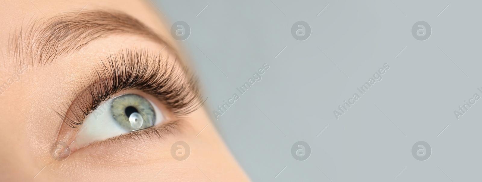 Image of Closeup view of young woman with beautiful long eyelashes on grey background, space for text. Banner design