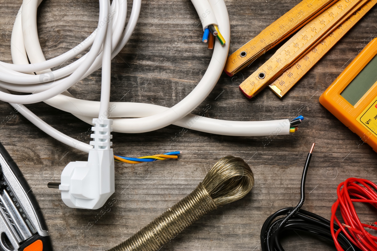 Photo of Wires and electrician's tools on wooden table, flat lay