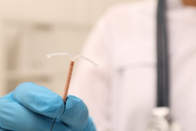Photo of Doctor holding T-shaped intrauterine birth control device on blurred background, closeup. Space for text