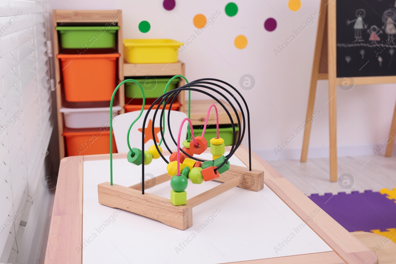 Photo of Toy bead maze on wooden table in playroom. Kindergarten interior design