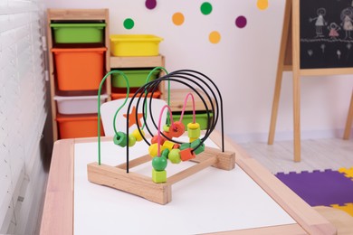 Toy bead maze on wooden table in playroom. Kindergarten interior design