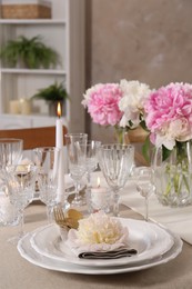 Stylish table setting with beautiful peonies and burning candles indoors