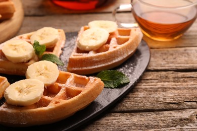 Photo of Tasty Belgian waffles with banana and mint on wooden table, closeup. Space for text