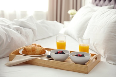 Photo of Tray with tasty breakfast on bed in light room