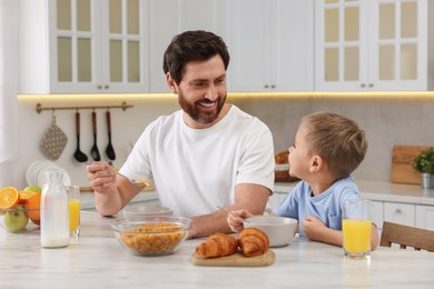 Photo of Father and his cute little son having breakfast at table in kitchen