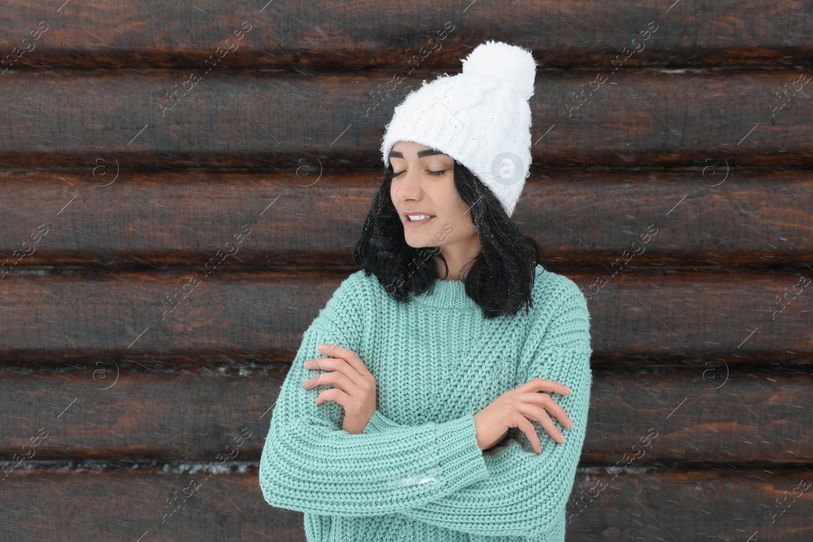 Photo of Young woman wearing warm sweater and hat near wooden wall. Winter season