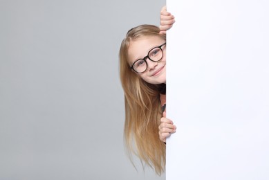 Photo of Cute girl looking out of placard on light grey background. Space for text